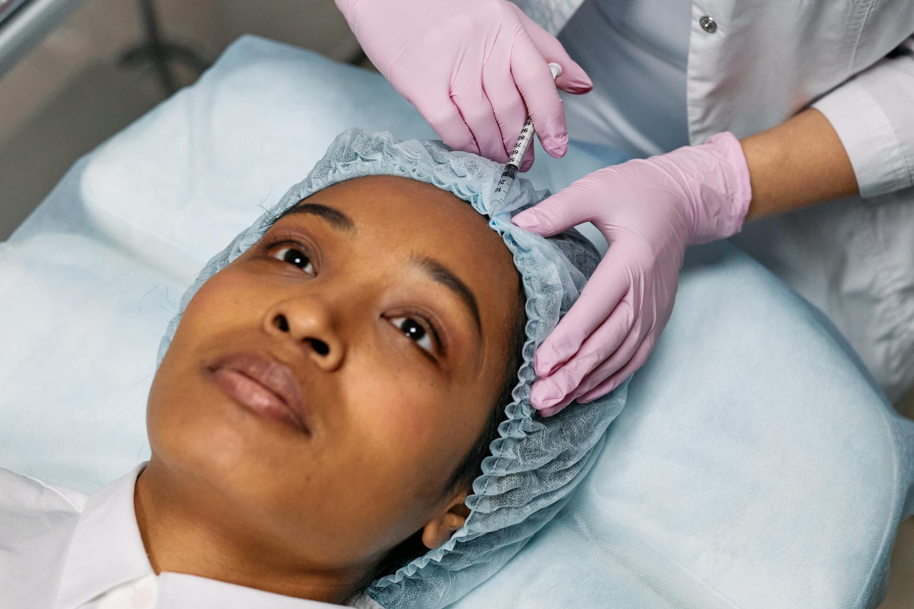 Profesional aplicando neuromodulador con jeringa fina en la frente de una paciente en clínica estética
